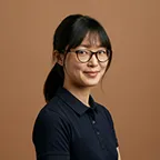 Portrait of a woman with glasses wearing a navy shirt against warm background.